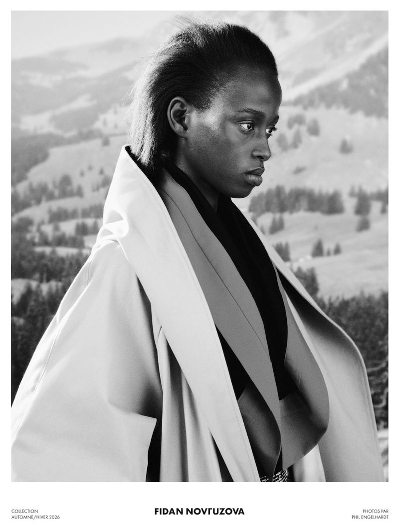 Model wearing a structured coat against a mountainous outdoor landscape background in a campaign image.