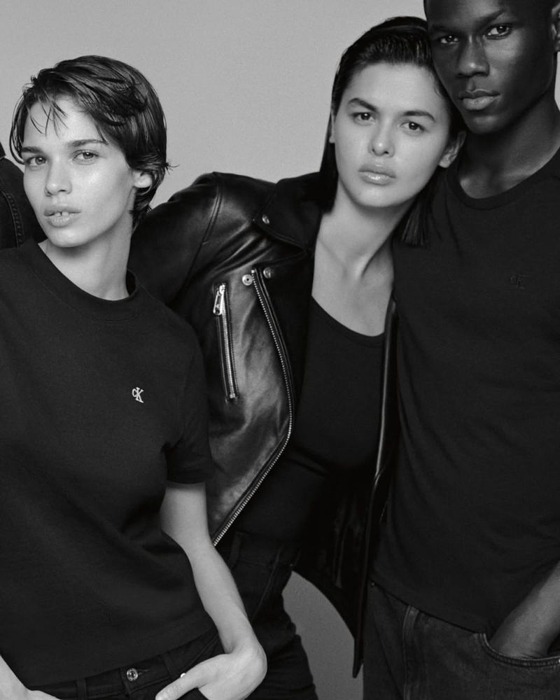 Black and white studio shot features three people modeling in casual clothing, one wearing a leather jacket, with neutral expressions.