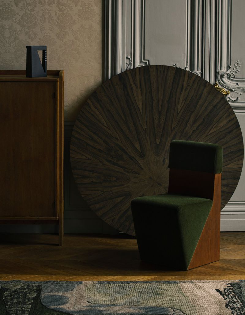 Green velvet upholstered chair in a room with wood flooring and a round wooden panel leaning against the wall