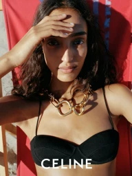 Model wearing a black bikini top and chunky gold necklace relaxing on a red sun lounger outdoors for Celine