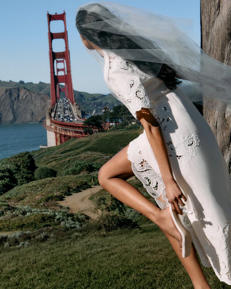 A woman in a white dress and veil poses on a grassy hill overlooking the Golden Gate Bridge.