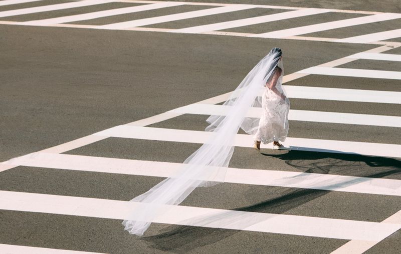 Model in a white dress with a long trailing veil walking across a zebra crossing for Cult Gaia