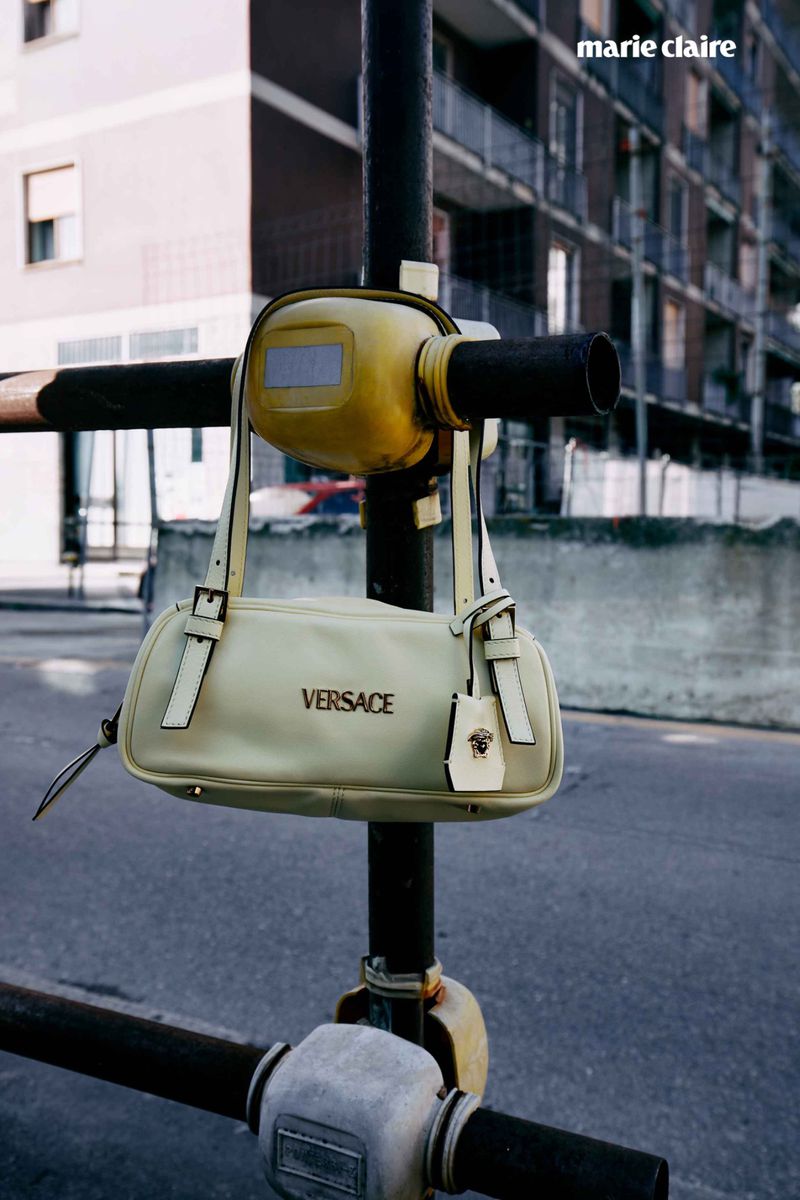 Versace handbag hanging on scaffolding against an urban building backdrop, neutral color palette, street scene, designer fashion.