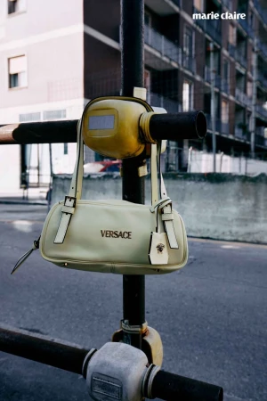 Versace handbag hanging on scaffolding against an urban building backdrop, neutral color palette, street scene, designer fashion.