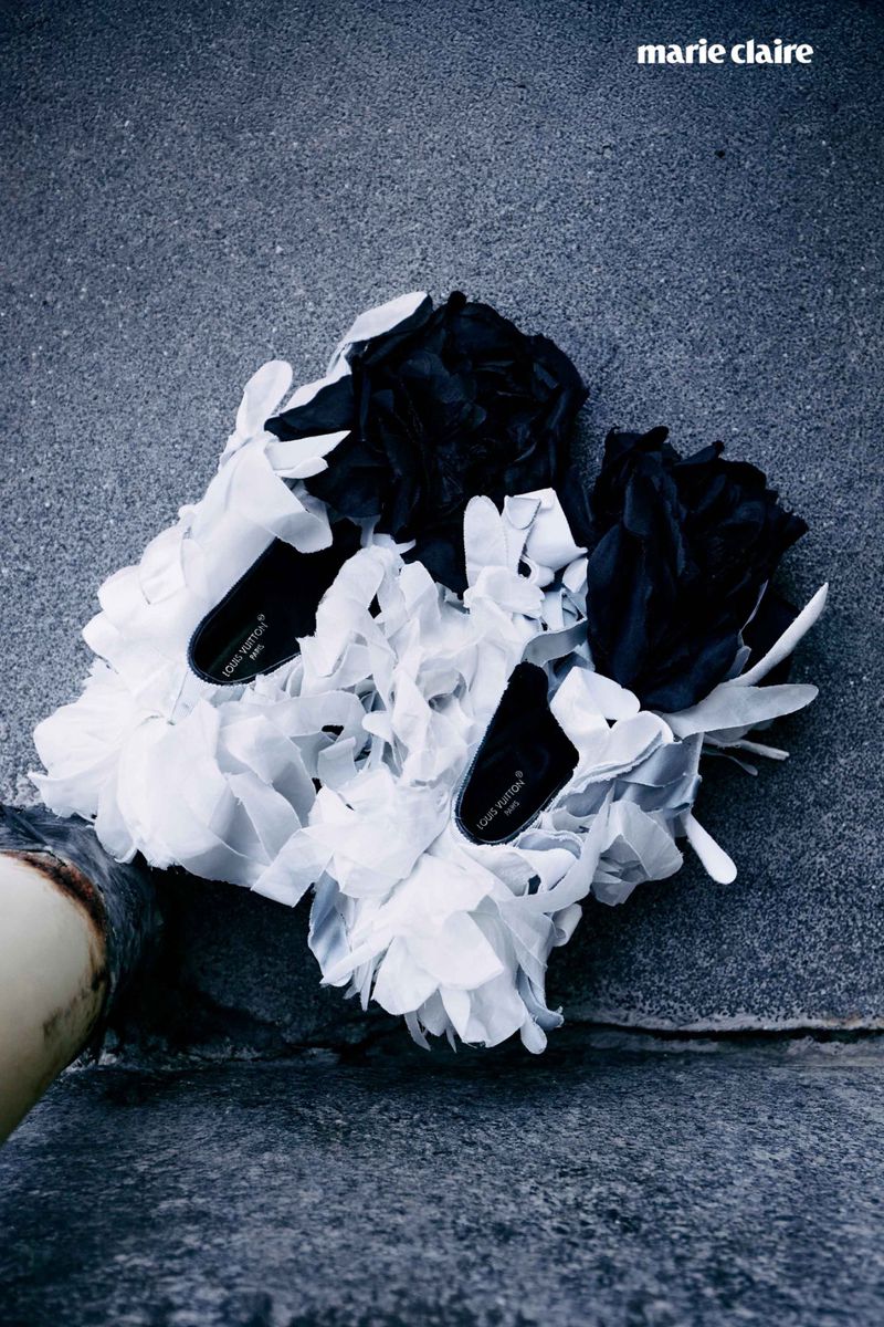Overhead fashion photography of two black and white flower-decorated shoes on a concrete surface with a magazine logo.