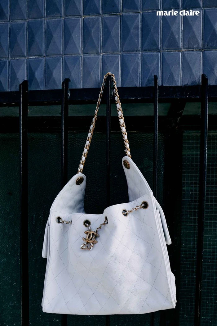 White quilted leather shoulder bag hanging on a black metal fence against a blue tiled wall for Marie Claire U.S.