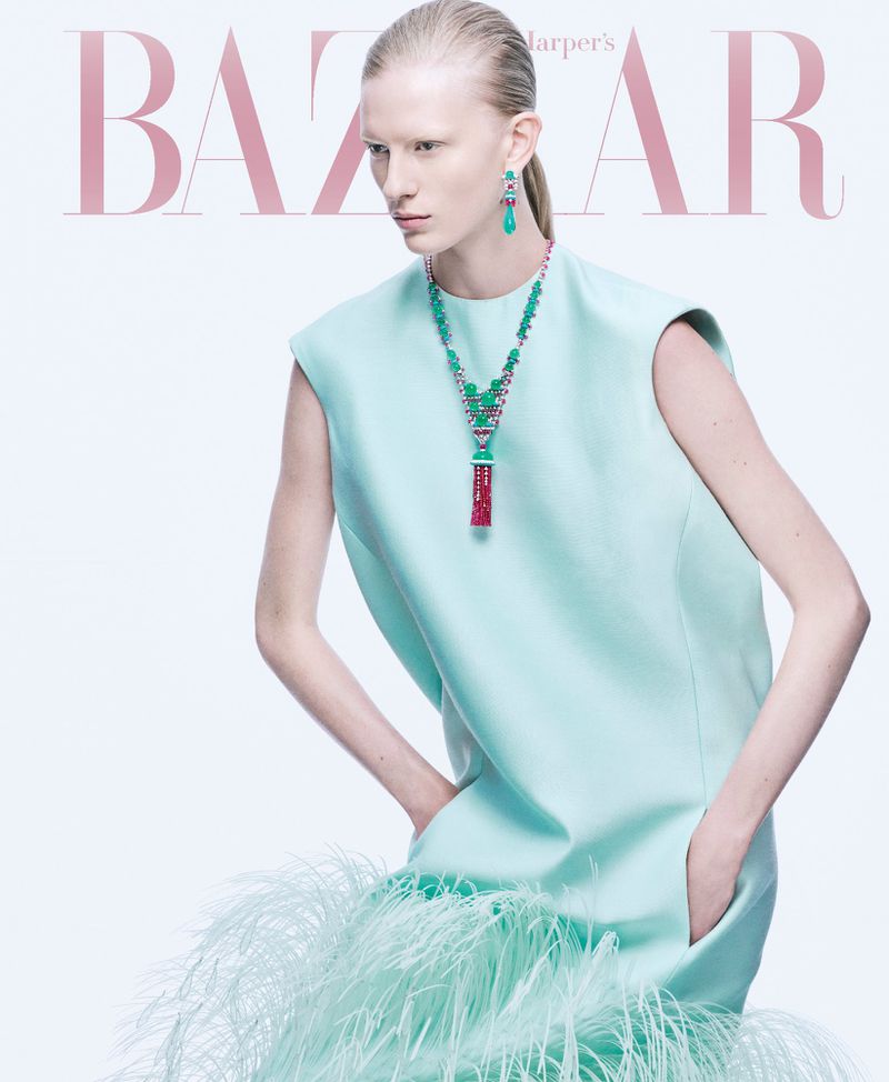 Model in mint green dress with feathered hem wearing statement jewellery against a white seamless background
