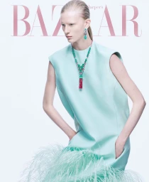 Model in mint green dress with feathered hem wearing statement jewellery against a white seamless background