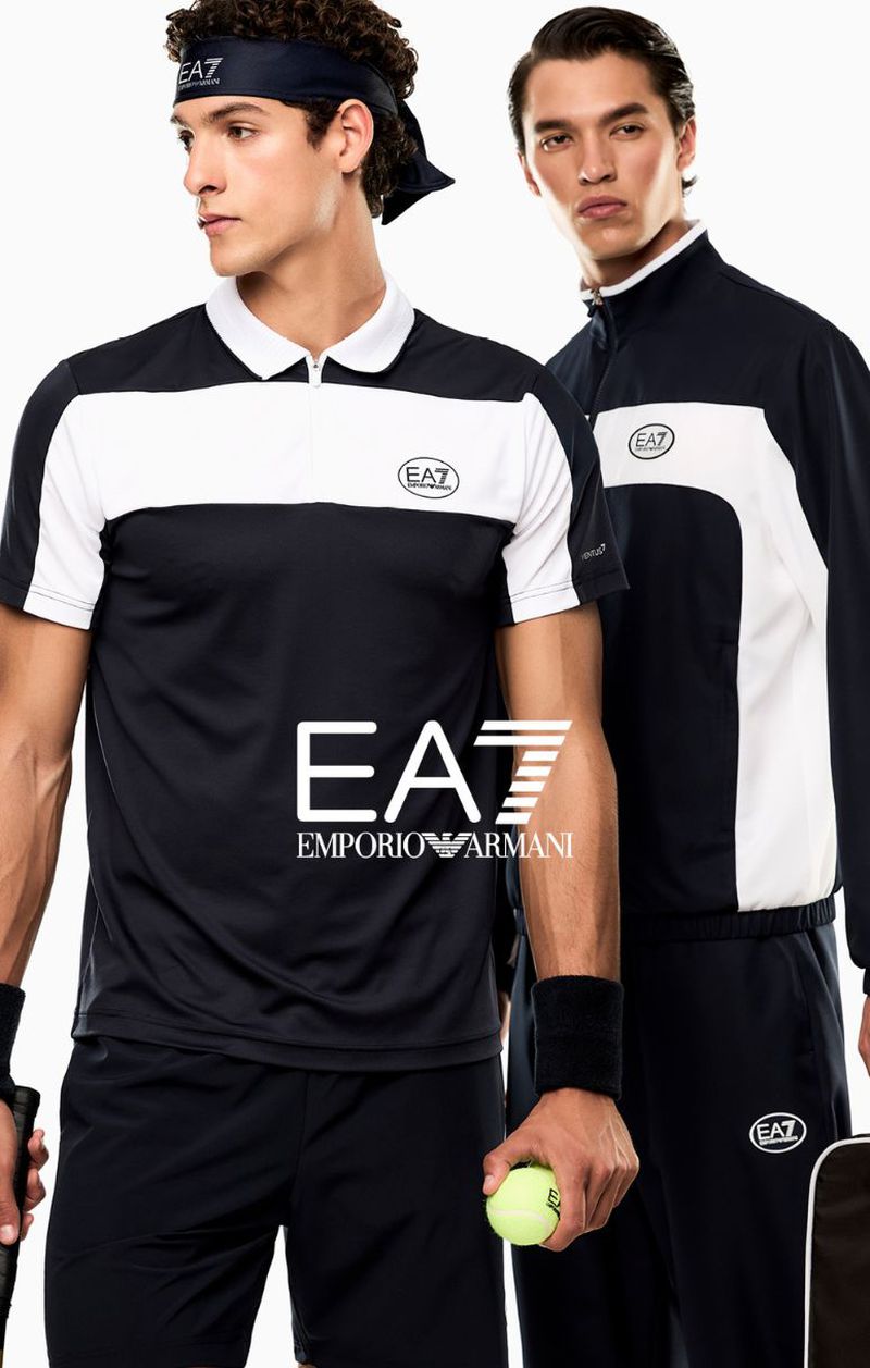 Two male models wearing Emporio Armani EA7 black and white sportswear against a white seamless background holding a tennis ball