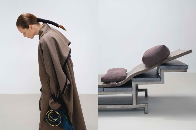Model in a brown coat with hair tied in a black wrap beside a modern stepped lounge chair with cushions.