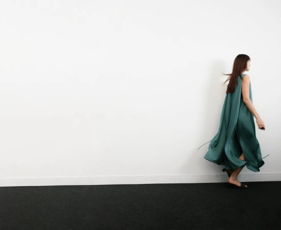 Model in a long flowing green dress walking across a minimalist studio setting with a white wall