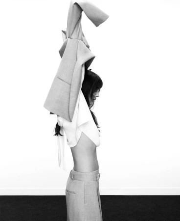 Model taking off a tailored blazer against a clean white studio background in a black and white fashion campaign image