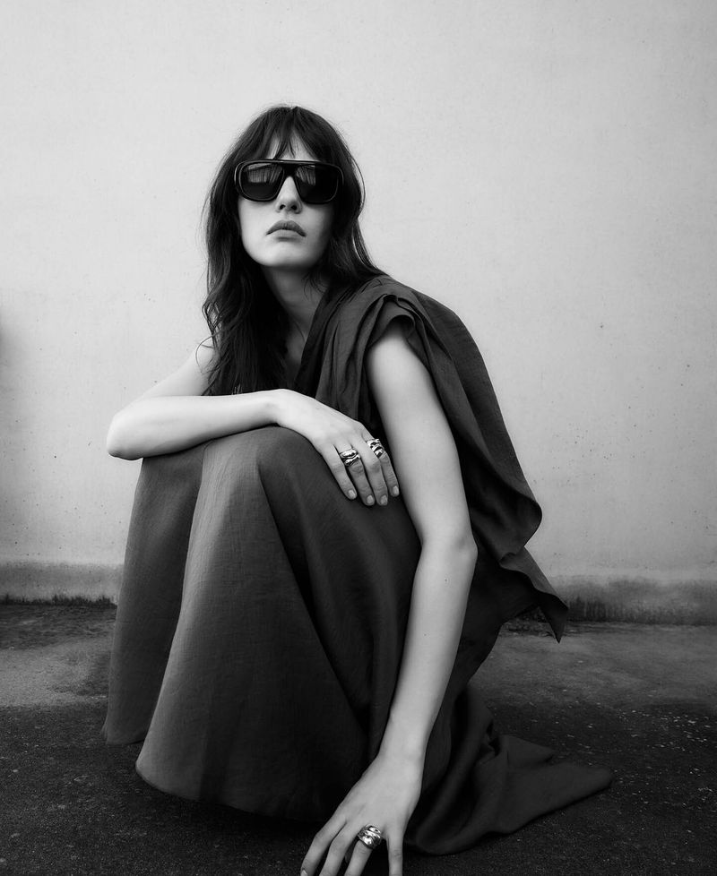 Model wearing dark sunglasses and draped apparel kneeling against a plain wall in this Adolfo Dominguez S/S 26 campaign image.