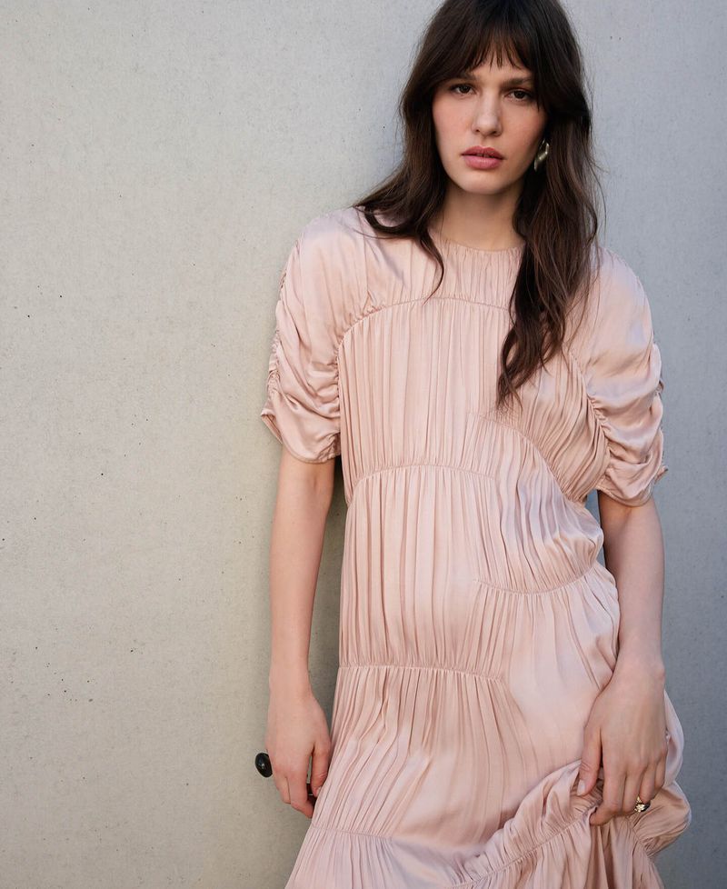 Model wearing a pleated pink dress posing against a plain grey concrete wall for Adolfo Dominguez SS26 campaign