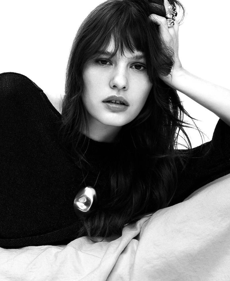 Model in black top with sculptural silver pendant and rings against white background for Adolfo Dominguez SS 26