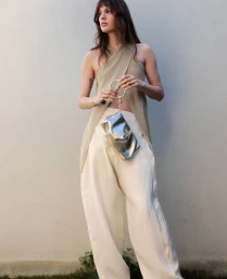 Model wearing a halter top and light trousers holding a metallic silver handbag against a plain wall for Adolfo Dominguez.