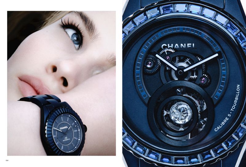 Close-up of an adult female model wearing a black Chanel watch against a blue backdrop, capturing a blend of fashion and technology.