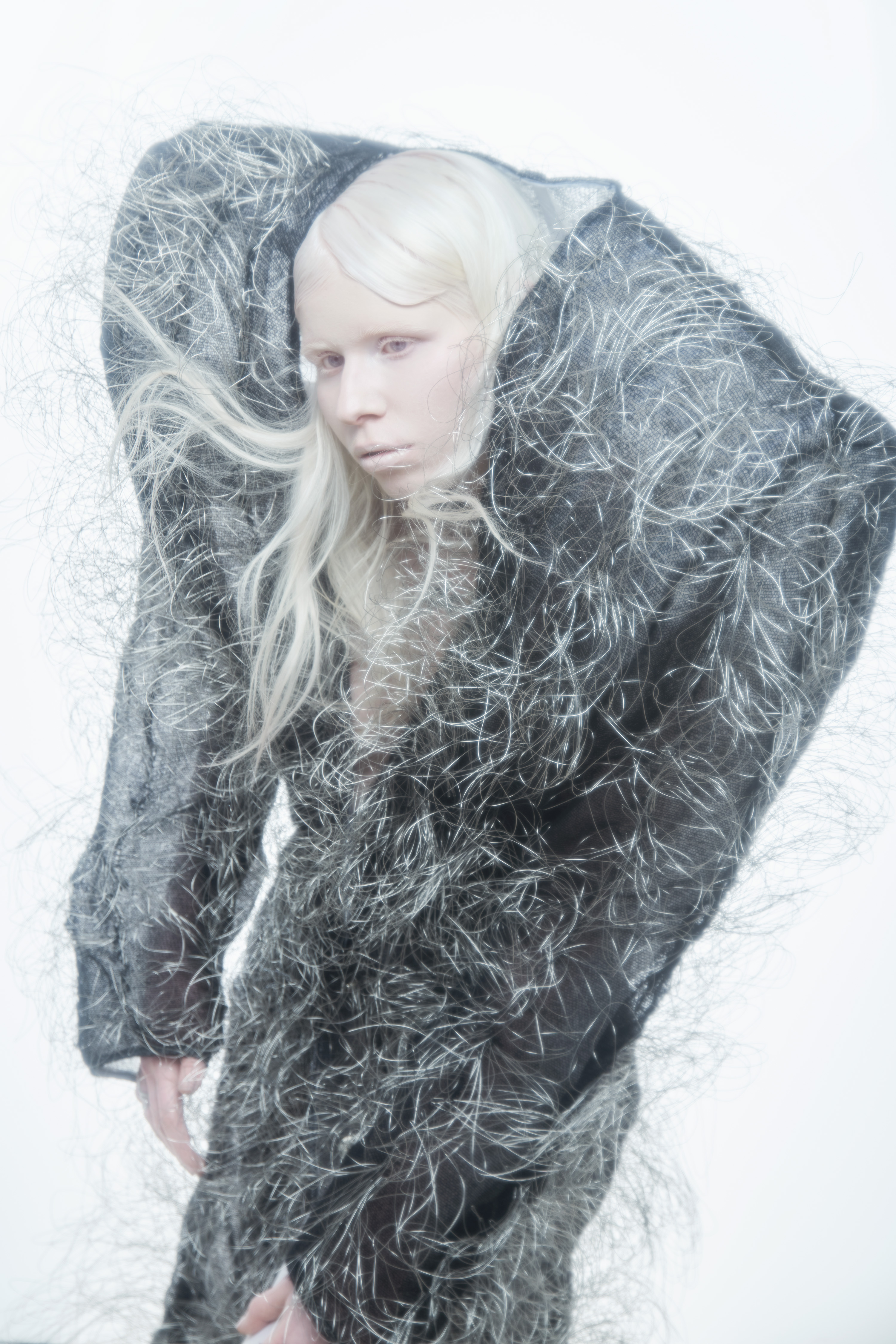 Model with long white hair wearing an oversized textured dark coat for Flanelle Magazine PLATINUM SIRENS