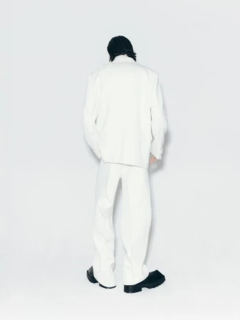 Back view of an adult male model in white suit and black shoes against a white background in a fashion studio setting.