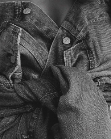 Close-up shot of a blue-gray folded denim jacket with button details, showcasing its texture and material in a monochromatic style.