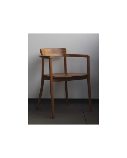 Studio shot of a light brown wooden armchair. Armchair has a seat, back, four legs, and armrests against a light grey background.