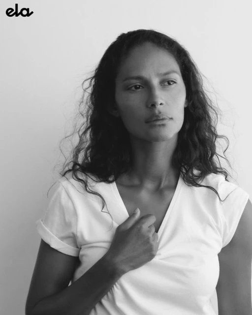 Portrait of a woman with wavy hair, wearing a white v-neck t-shirt, against a white background in a black and white studio shot.