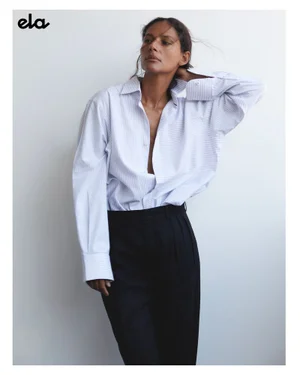 Model Emanuela de Paula wearing a pinstripe button-down shirt and dark trousers against a white seamless background