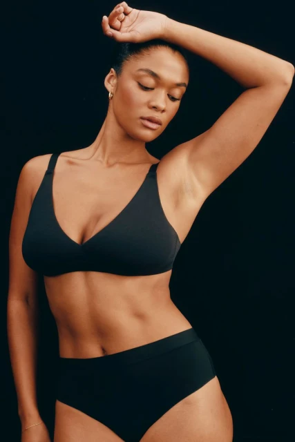 Portrait of a black female adult with dark hair in black underwear and bra posing in front of a dark background in a photo studio.
