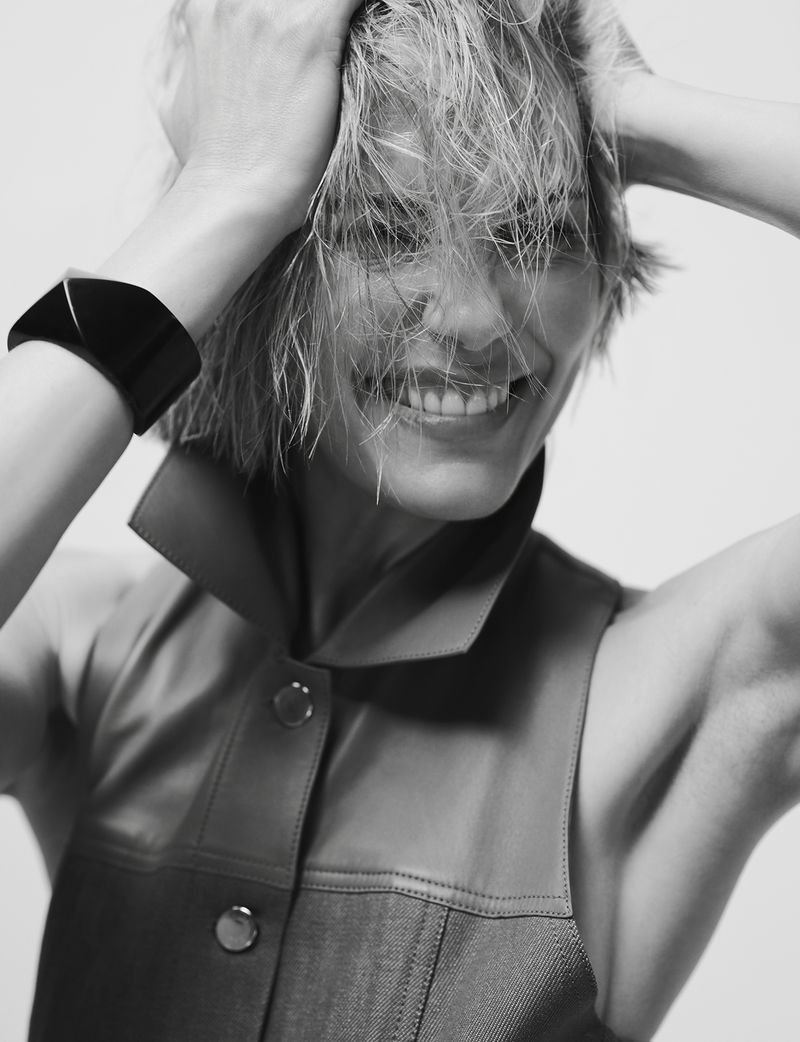 Black and white portrait of a smiling adult female with wet blonde hair, wearing a sleeveless button-down, and a thick black bracelet.