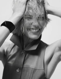 Portrait of Leslie Bibb smiling with wet hair, wearing a structured sleeveless top and a large black cuff bracelet.