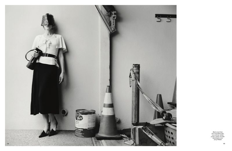 A woman in a surreal black-and-white fashion photograph with a bizarre head covering, posing near construction site objects.