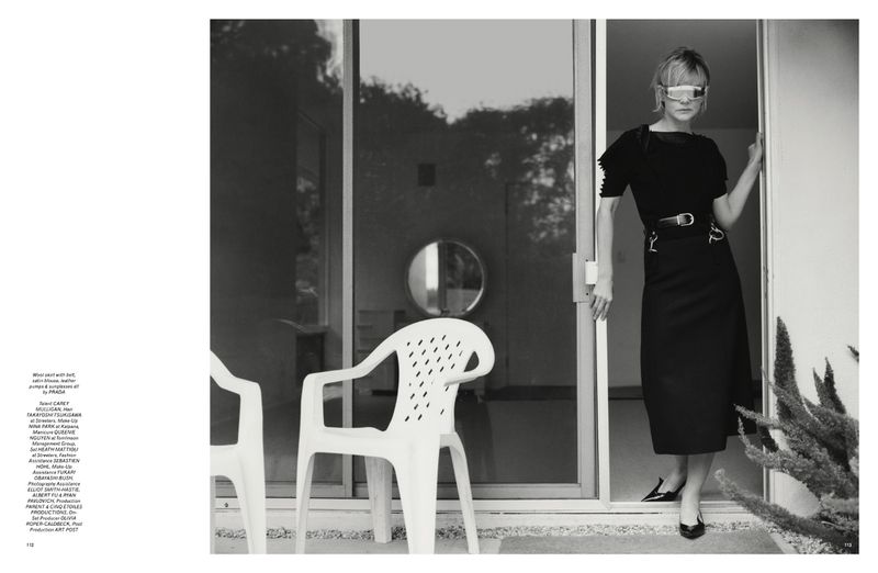 Indoor shot of an adult female model with visor sunglasses, posing in a black dress, entering a building with white plastic chairs.