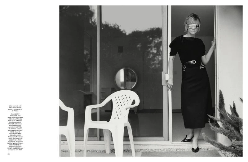 Indoor shot of an adult female model with visor sunglasses, posing in a black dress, entering a building with white plastic chairs.
