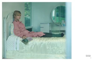 Carey Mulligan in a pink trench coat reclining on a bed in a light-filled bedroom for Pop Magazine by Thurstan Redding