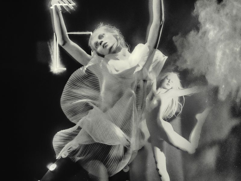 Monochrome portrait of a fair-skinned woman in a pleated dress, captured in a long exposure shot with abstract lighting effects.