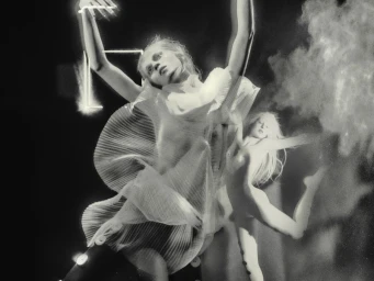 Model in ruffled white sheer dress posing dynamically amidst glowing light elements and powder smoke for Evade House project.