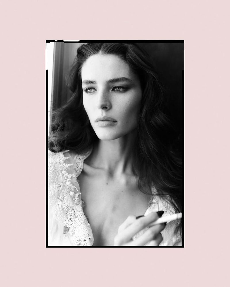 Black-and-white portrait of a beautiful woman with dark hair and smokey eyes, wearing a lace top and holding a cigarette.