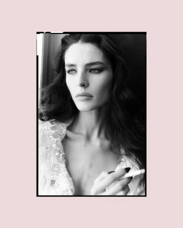 Black-and-white portrait of a beautiful woman with dark hair and smokey eyes, wearing a lace top and holding a cigarette.
