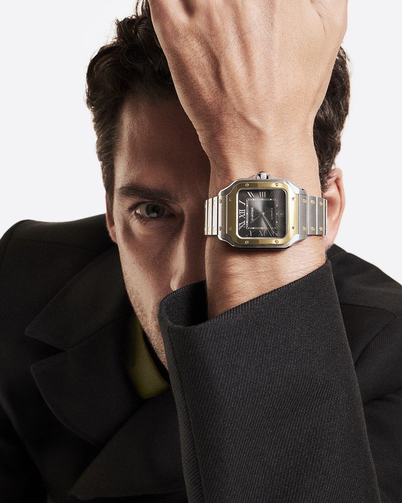 Close-up studio shot of an adult male model showcasing a two-tone wristwatch with a square black dial and Roman numeral markers.