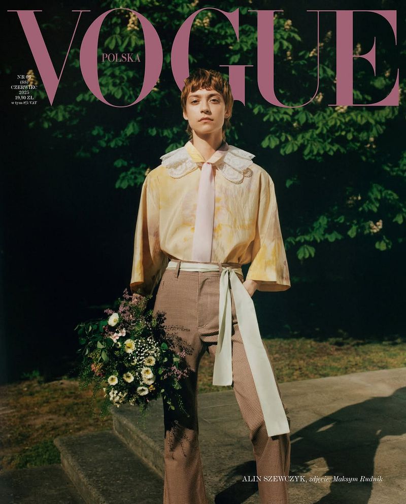 Vogue Polska magazine cover featuring Alin Szewczyk in a yellow patterned shirt, brown pants, holding flowers, standing outdoors.