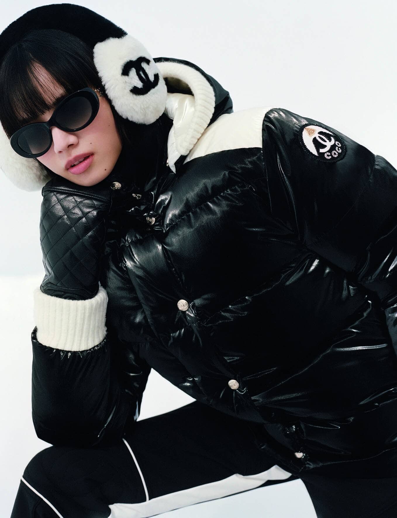 Model Nana Komatsu wearing a black and white Chanel puffer jacket, earmuffs, and sunglasses against a white background