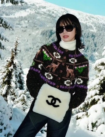 Nana Komatsu wearing patterned knitwear and holding a white fluffy handbag against a snowy mountain landscape.