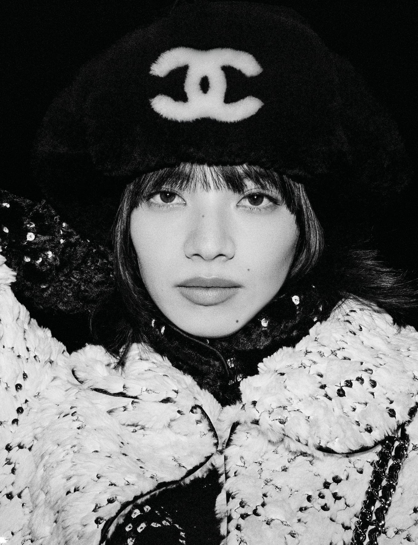 Close-up black and white portrait of model Nana Komatsu wearing a fuzzy winter hat with Chanel logo and textured jacket