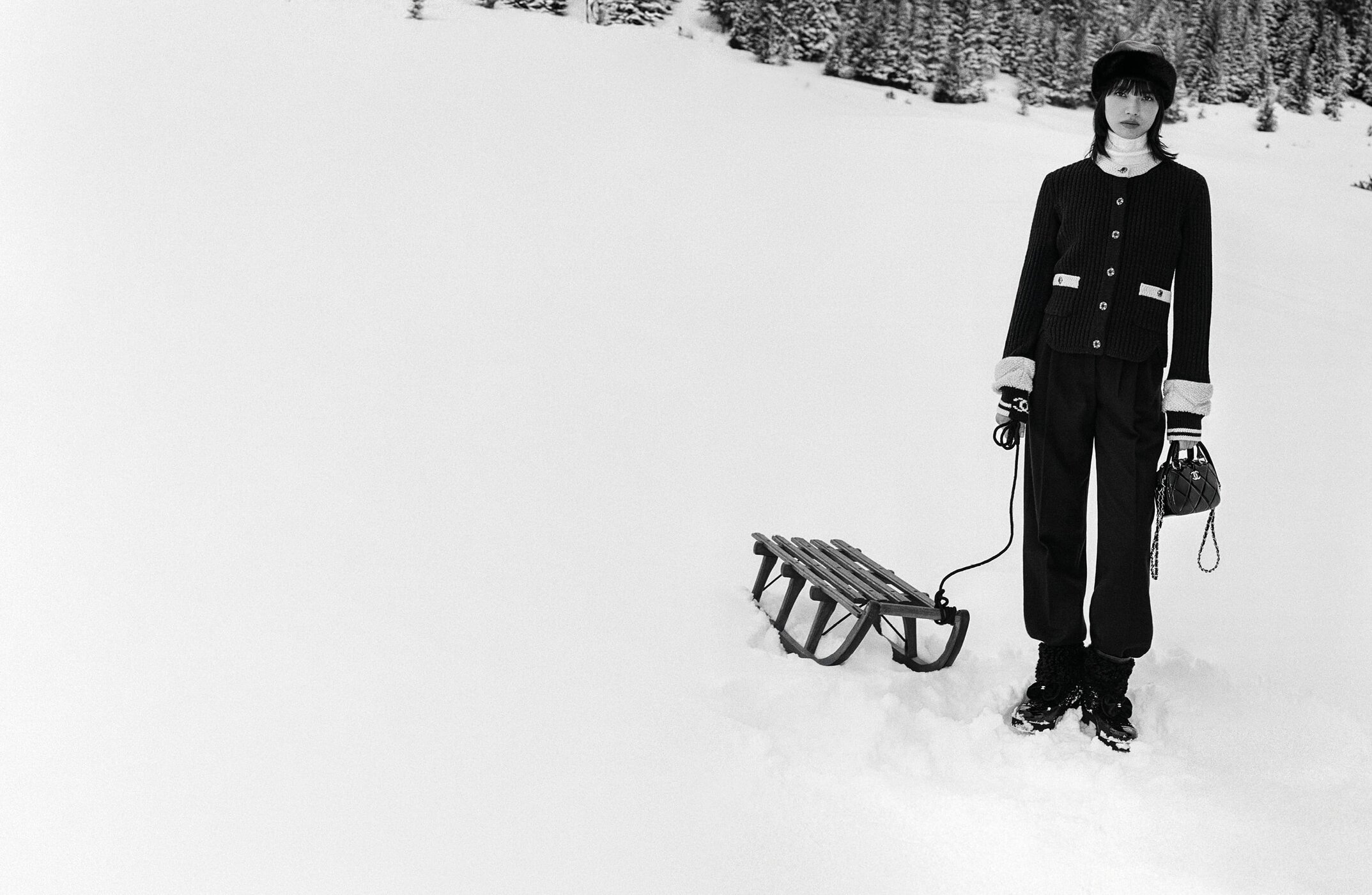 Nana Komatsu wearing Chanel winter apparel standing in snow next to a wooden sled for Coco Neige campaign