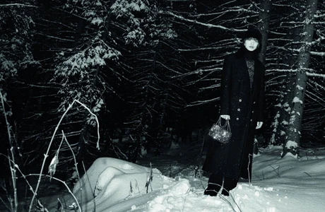 Nana Komatsu wearing a dark coat and winter hat standing in a snowy forest at night for the Chanel Coco Neige 2025 campaign.