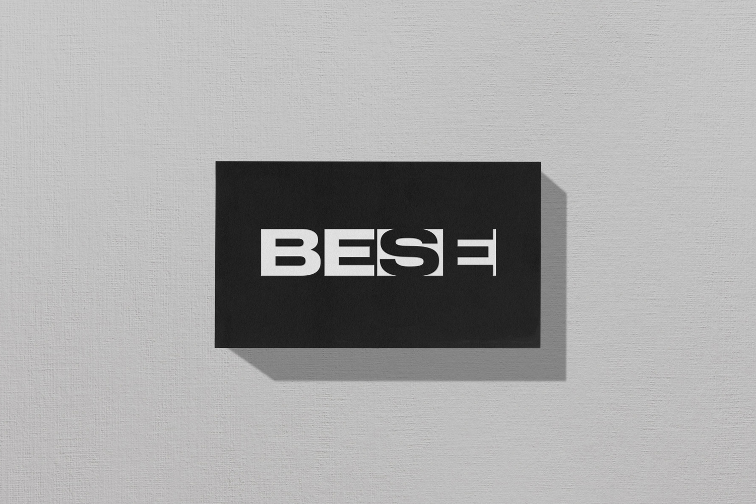 Black rectangular brand identity card featuring bold white BESE logo text resting on a light grey textured surface.