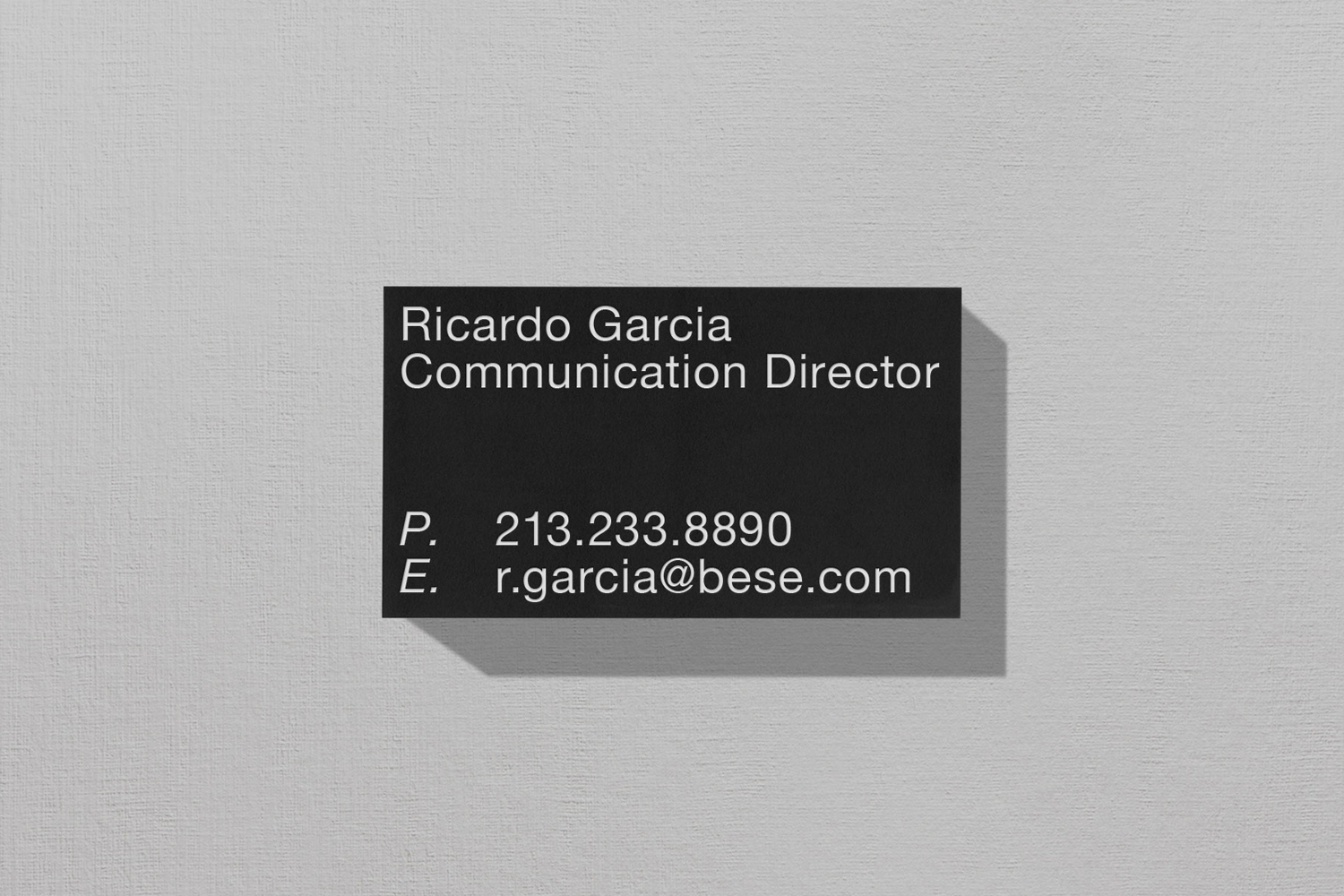 Black business card with white sans-serif typography resting on a textured light grey paper background