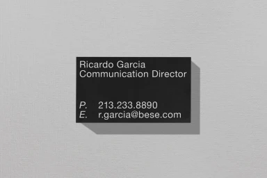 Black business card with white sans-serif typography resting on a textured light grey paper background