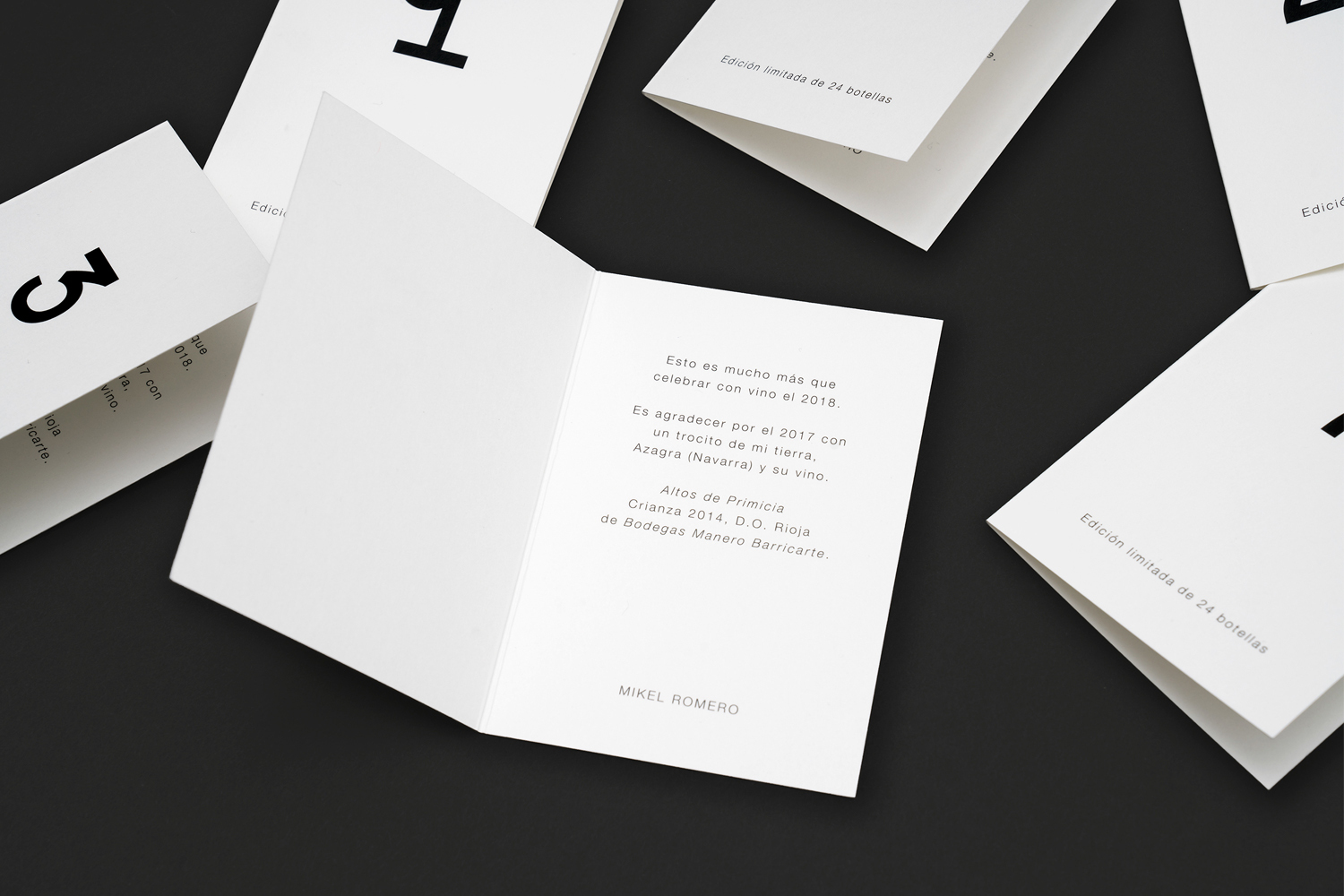 Minimalist white folded cards with black typography arranged flat on a dark surface
