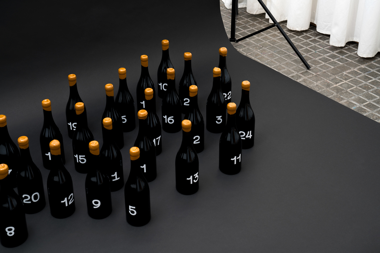 Arrangement of black numbered bottles with gold caps on a grey seamless studio sweep background.
